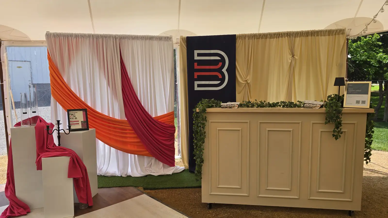 Our open house booth: sheer white walls with orange and red accent swags, three white pillars and a cream wall behind the Bar-Key bar