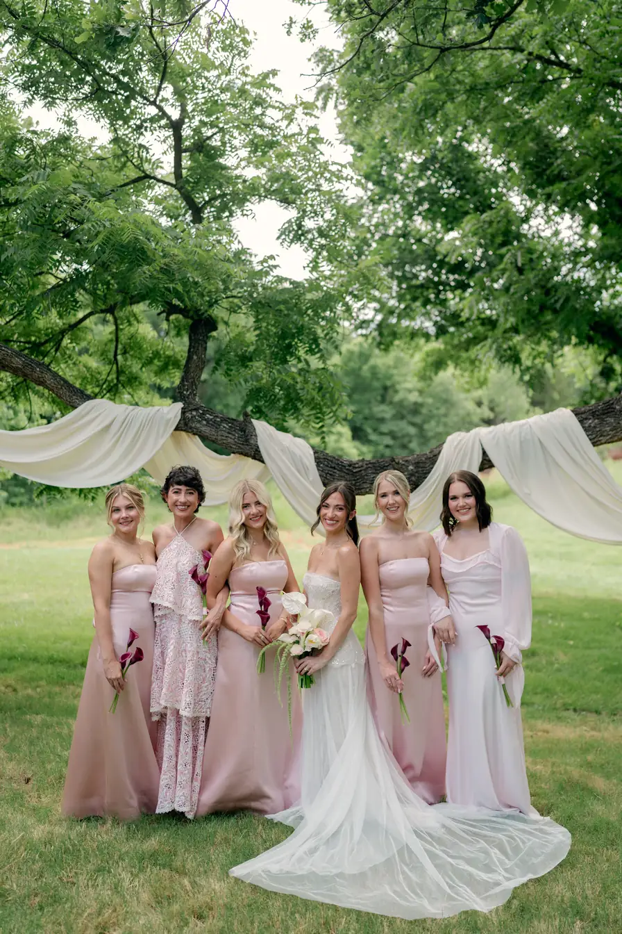 The bridal party in blush gowns under the draped tree line