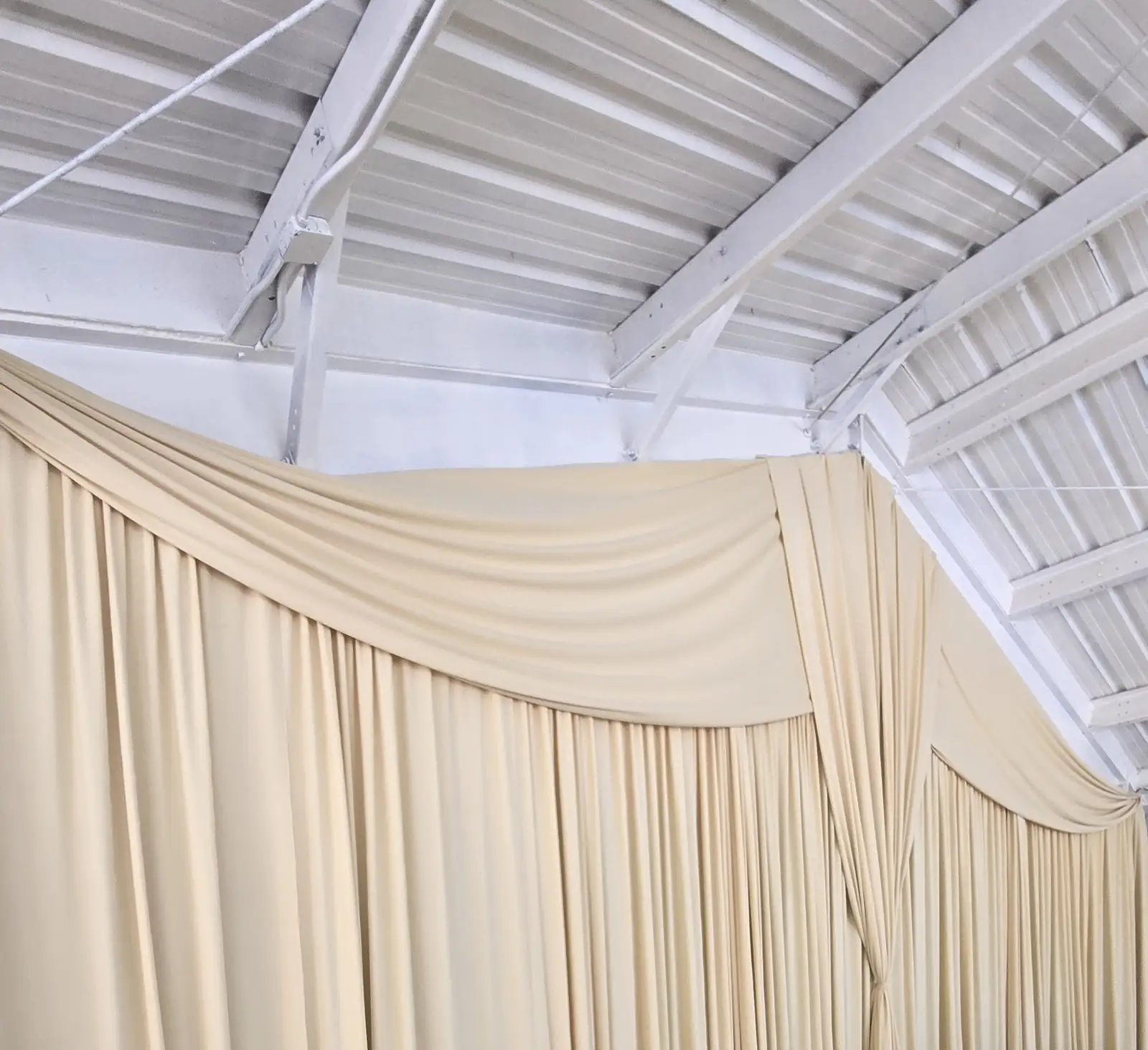 The cream drape wall with a gathered swag and a tied center, hung behind the head table